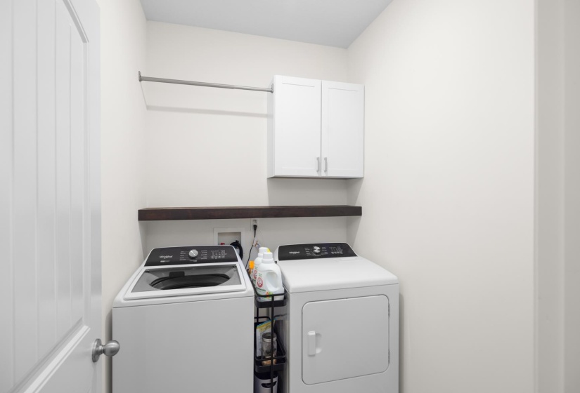 Dedicated laundry area featuring a white shaker-style cabinet, a dark wood-finish floating shelf, and a chrome hanging rod