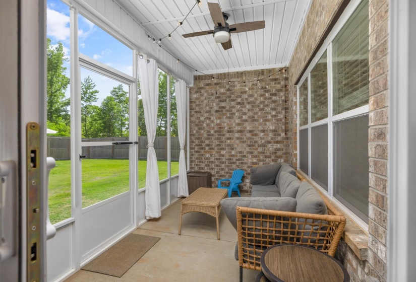 Screened-in patio featuring a concrete floor, brick wall, ceiling fan, and string lighting