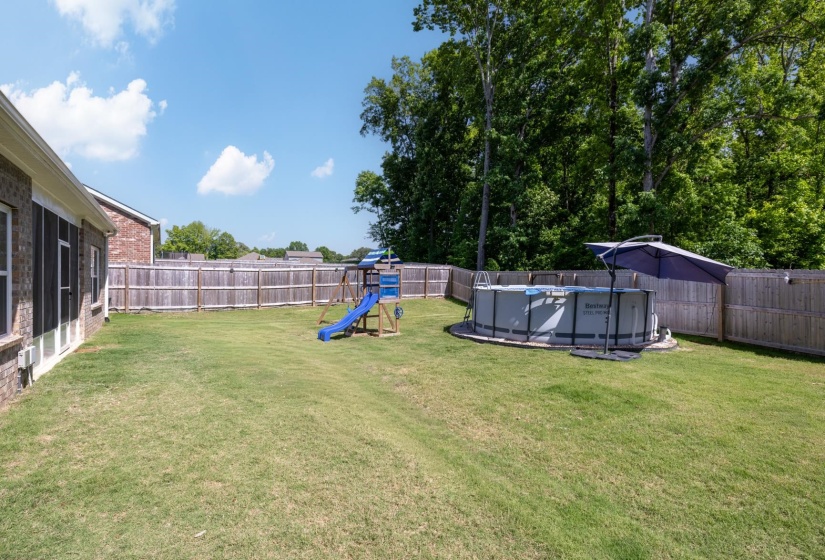 Expansive backyard featuring a fenced perimeter, brick exterior, and a wood-finish playset