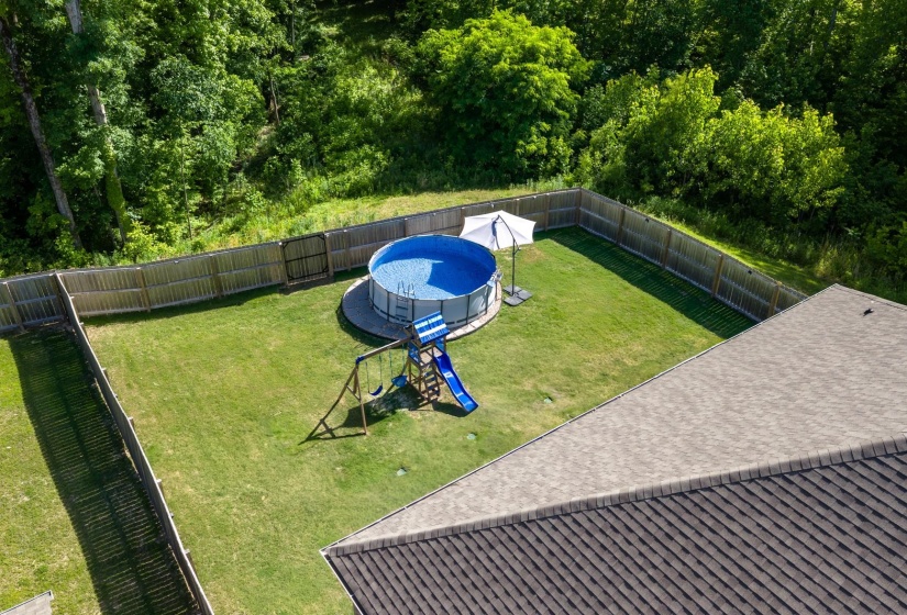 Fenced backyard featuring an above-ground pool on a gravel base, a swing set with a slide, and a manicured lawn
