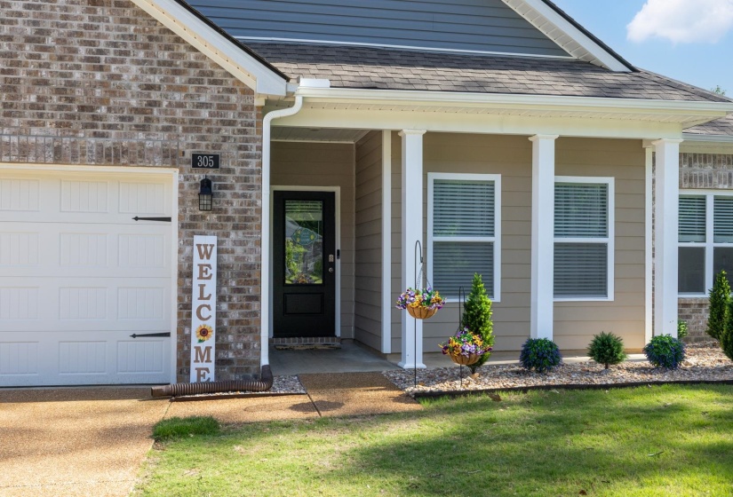 Exterior featuring brick and siding finishes, a covered entry with columns, a black front door with glass paneling, a two-car garage with decorative hardware, and foundational landscaping