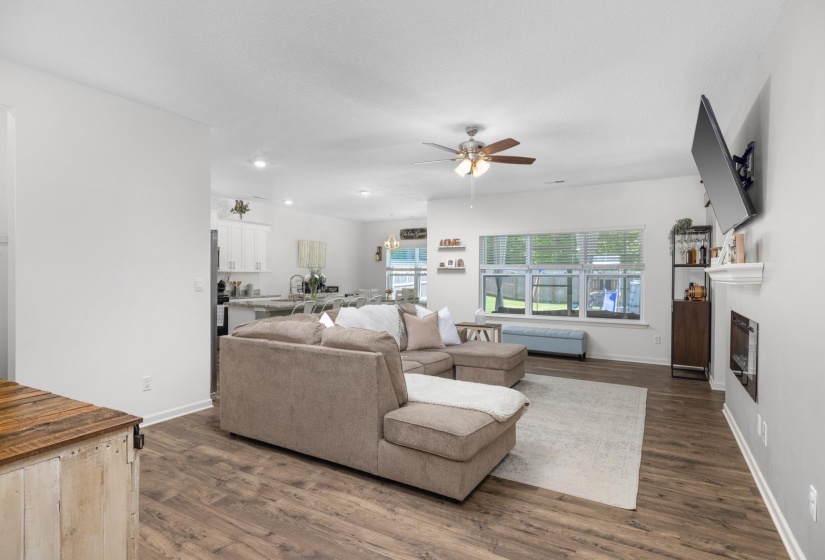 Open-concept living area featuring wood-finish flooring, a ceiling fan, recessed lighting, and a built-in fireplace with a mantel