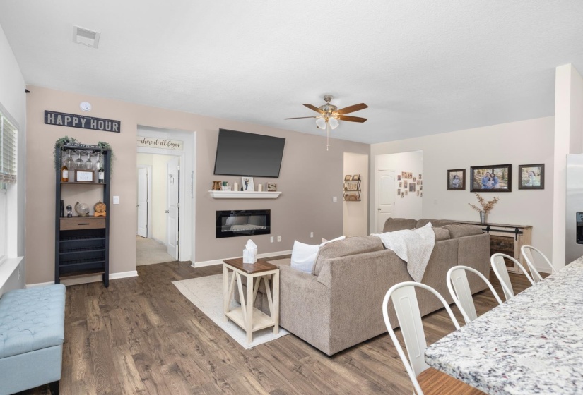 Open-concept living space featuring wood-finish flooring, a contemporary electric fireplace with a mantel, and a ceiling fan