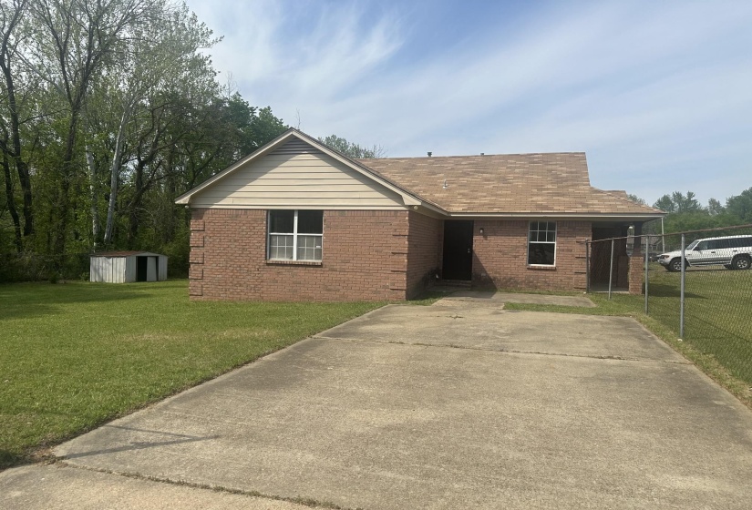 Brick exterior with tan siding features a brown shingle roof, a concrete driveway, and a chain-link fence