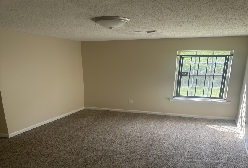 Room featuring wall-to-wall carpeting, light neutral wall paint, and a window with security bars