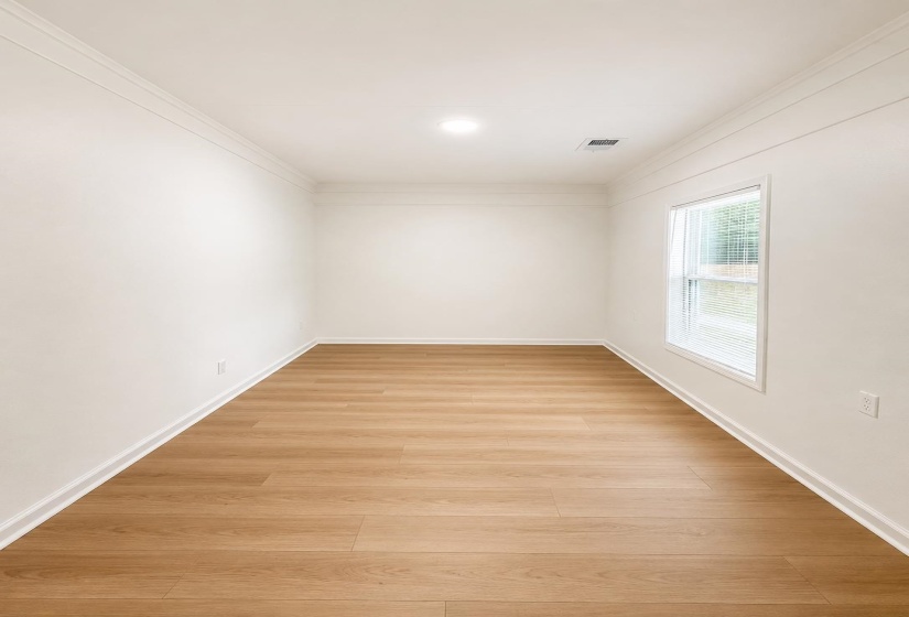 Room featuring wood-finish flooring, crisp white walls, crown molding, and a single window with horizontal blinds