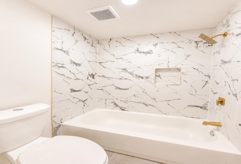 White subway tile bathtub surround with black veining, integrated shower niche, and gold-finish fixtures
