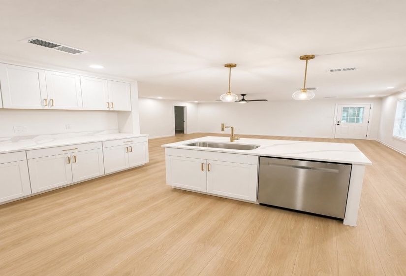 Modern kitchen featuring white cabinetry with gold-finish hardware, quartz countertops, and a stainless steel dishwasher
