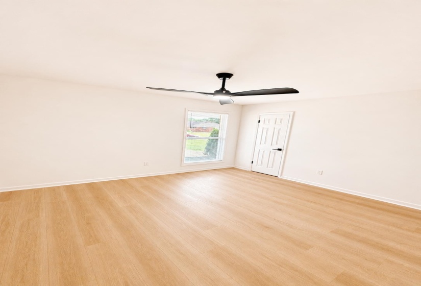 Light-filled room featuring wood-finish flooring, a modern black ceiling fan, white baseboards, and a paneled white door with black hardware