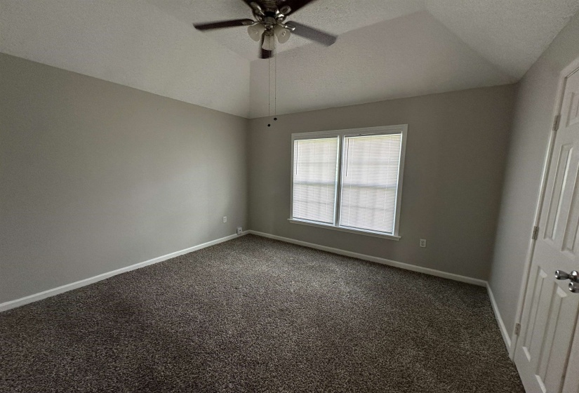 Spare room with ceiling fan, dark colored carpet, and vaulted ceiling