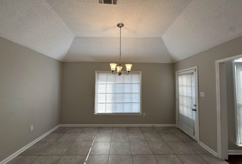 Unfurnished dining area featuring a chandelier, tile patterned flooring, lofted ceiling, and a textured ceiling