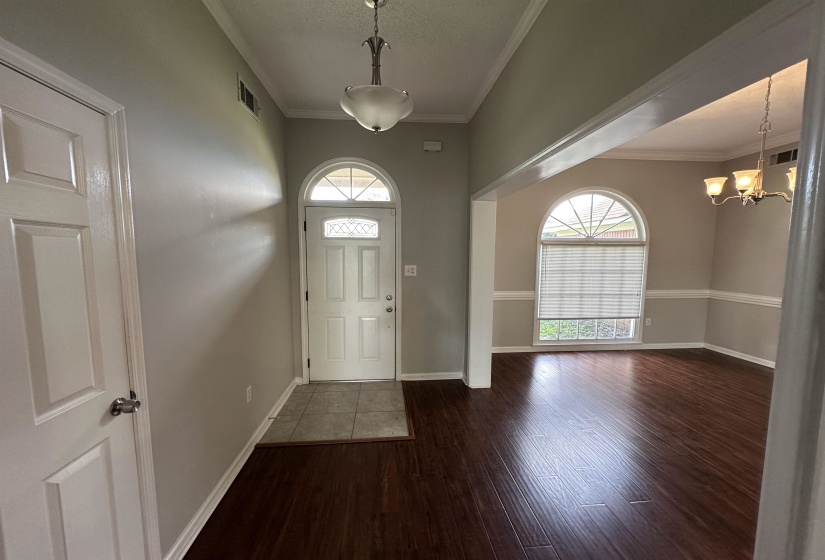 Entryway featuring dark wood-style flooring, plenty of natural light, a chandelier, and ornamental molding