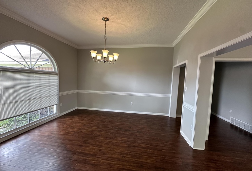 Empty room featuring a chandelier, a textured ceiling, wood finished floors, and ornamental molding