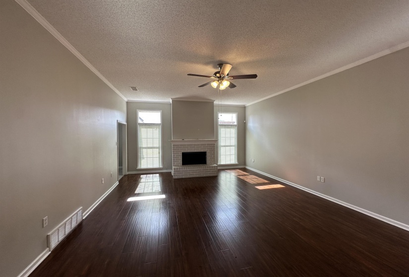 Unfurnished living room with a textured ceiling, ceiling fan, dark wood-style flooring, a fireplace, and crown molding