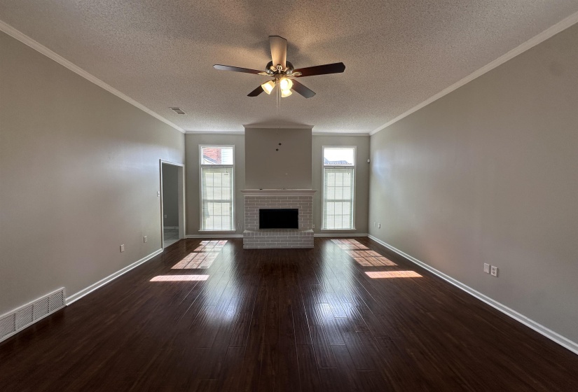 Unfurnished living room featuring a textured ceiling, a ceiling fan, dark wood-style flooring, crown molding, and a fireplace