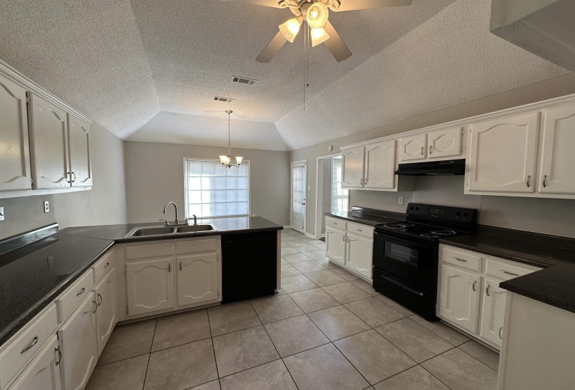 Kitchen with black appliances, under cabinet range hood, a peninsula, lofted ceiling, and white cabinetry