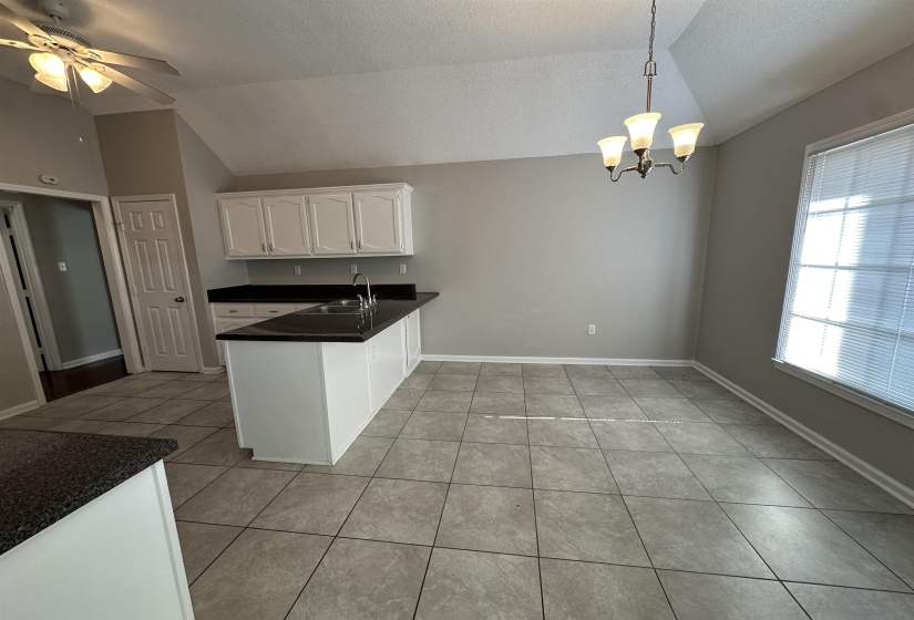 Kitchen with lofted ceiling, a peninsula, white cabinetry, dark countertops, and light tile patterned flooring