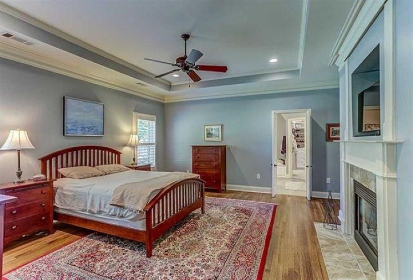 Bedroom with light wood-style flooring, a fireplace with flush hearth, a tray ceiling, and ornamental molding