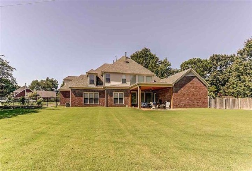 Rear view of house featuring brick siding, fence, and a lawn