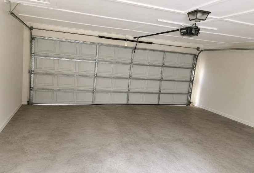 Garage interior featuring a sectional white panel door, concrete flooring, white painted walls, and a ceiling-mounted light fixture