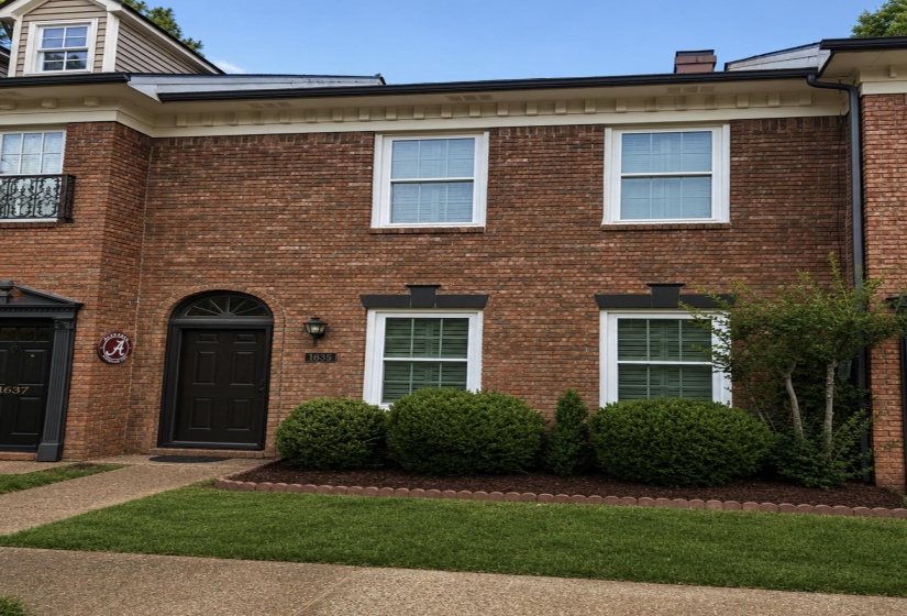 Brick-front residence featuring a dark wood arched entry door, white trim windows, and decorative planters