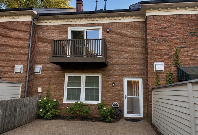 Brick exterior featuring a private balcony with a wooden railing, a glass-paneled door, and a white-framed window