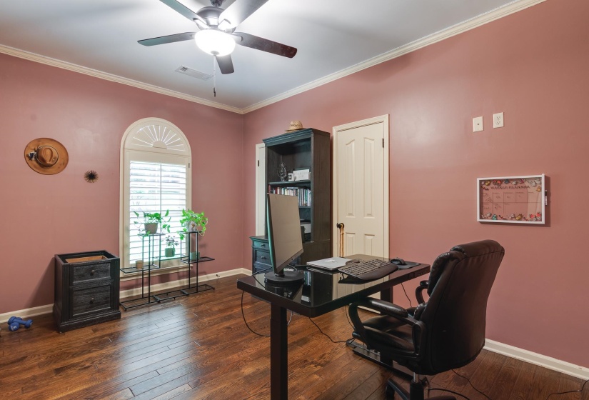 Arched window with plantation shutters, wood-finish flooring, crown molding, ceiling fan with light fixture, and a paneled interior door