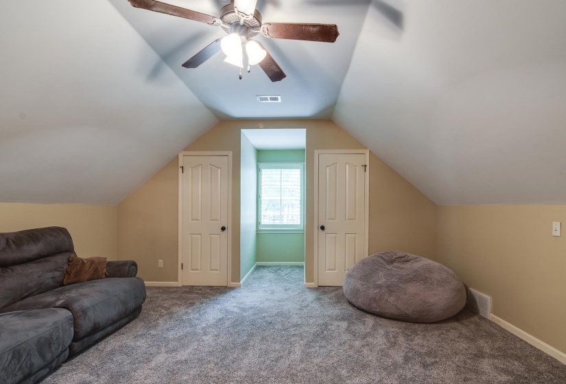 Spacious bonus room featuring sloped ceilings, plush gray carpeting, a built-in window nook, and two paneled doors