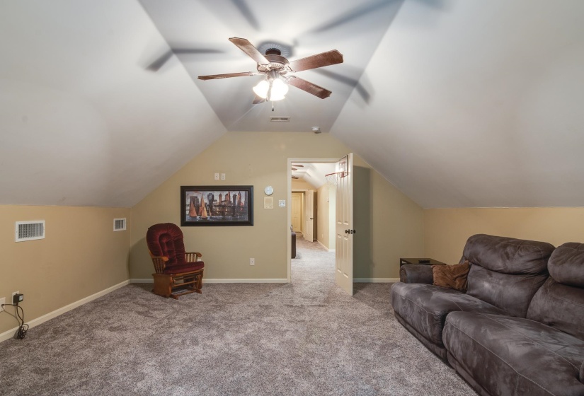Carpeted bonus room featuring a ceiling fan with integrated lighting, sloped ceilings, and neutral wall tones