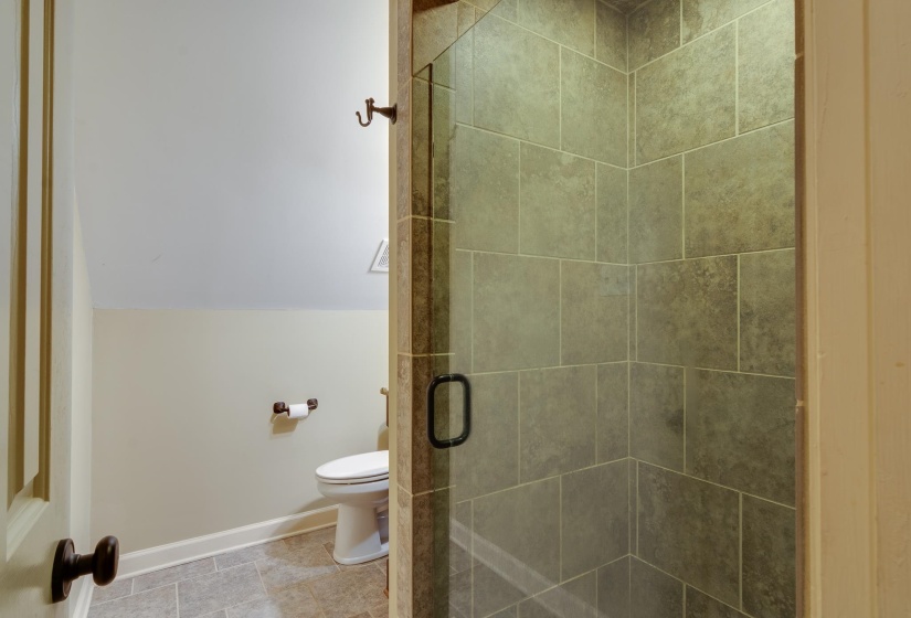 Bathroom featuring a glass-enclosed shower with tile surround, a white toilet, and tile flooring