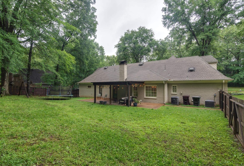 Expansive rear yard featuring a covered patio, brick exterior, and partial perimeter fencing