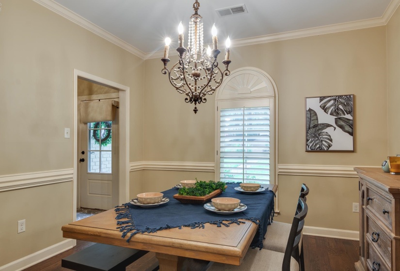Dining area featuring a decorative chandelier, crown molding, chair rail, arch-top window with plantation shutters, and wood-finish flooring