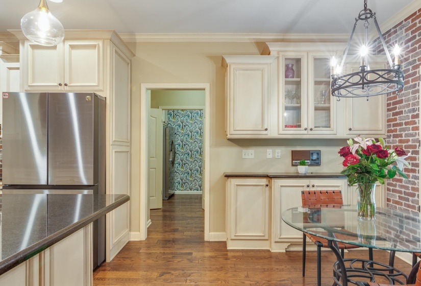 Kitchen featuring wood-finish flooring, cream-toned cabinetry with glass-front accents, and a stainless steel refrigerator