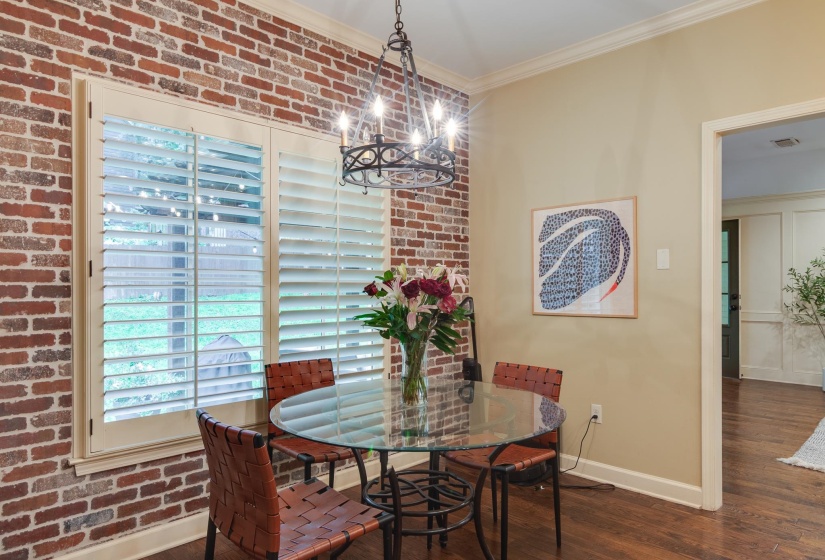 Exposed brick wall featuring white plantation shutters and crown molding