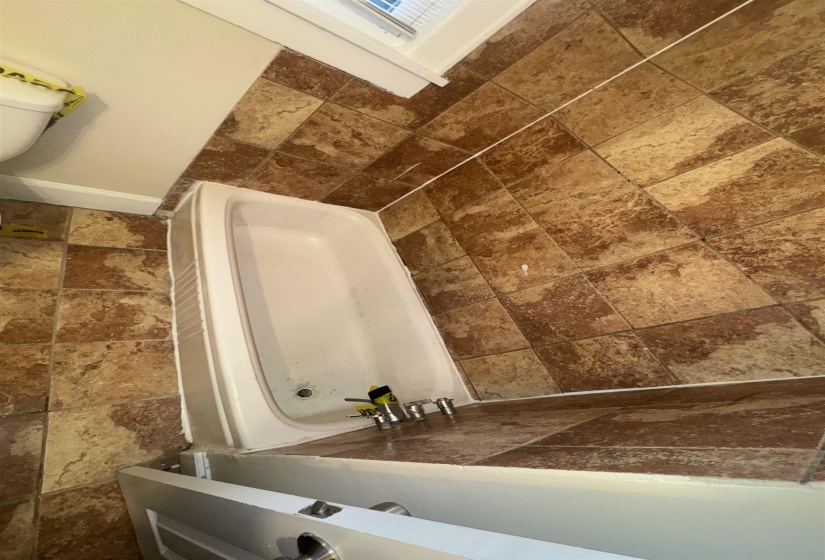 White bathtub with a chrome faucet set, surrounded by brown-toned tiled walls and flooring