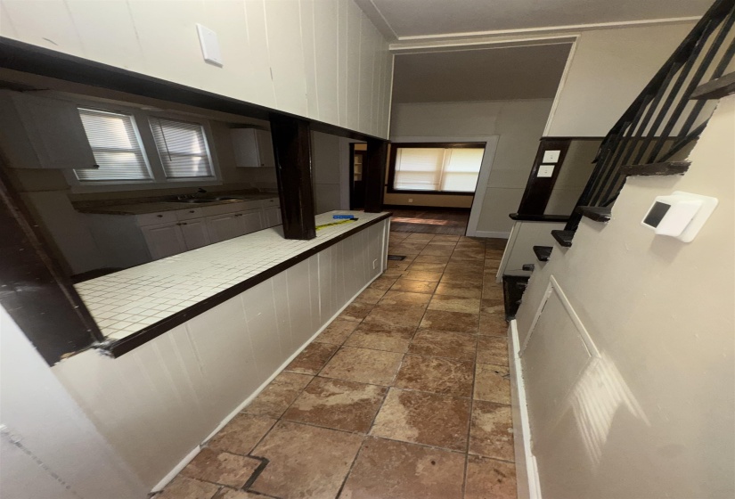 Tiled flooring extending through a central hallway, featuring a pass-through window to the kitchen with white cabinetry and a double basin sink