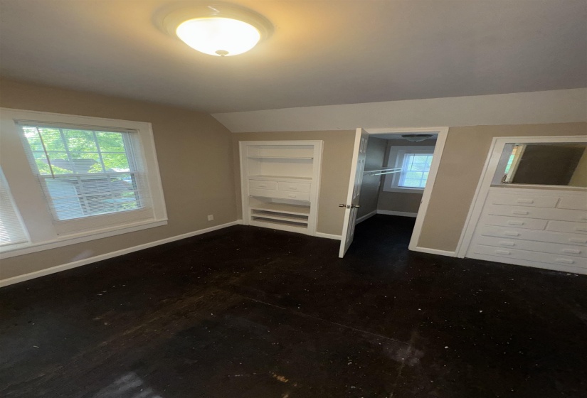 Room featuring dark wood-finish flooring, two windows with blinds, a built-in shelving unit, and a built-in dresser