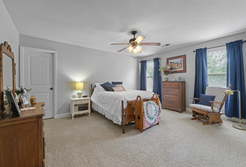Spacious bedroom with plush carpet, calming neutral tones, ceiling fan, and plenty of room to relax.