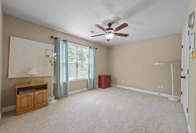 Bright and inviting secondary bedroom featuring soft neutral colors, large window for natural light, ceiling fan, and generous floor space for flexible furniture placement.