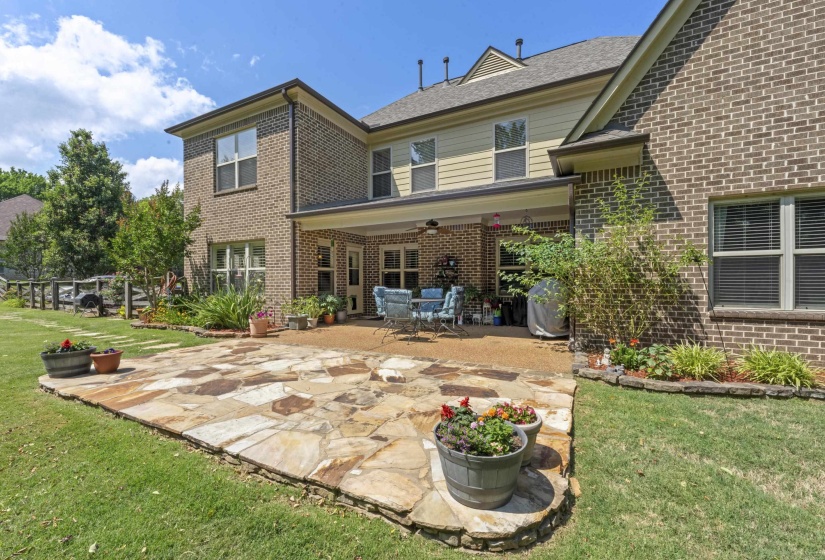 Beautiful backyard retreat featuring an expansive stone patio, covered entertaining area, mature landscaping, and plenty of room for gatherings and outdoor enjoyment.