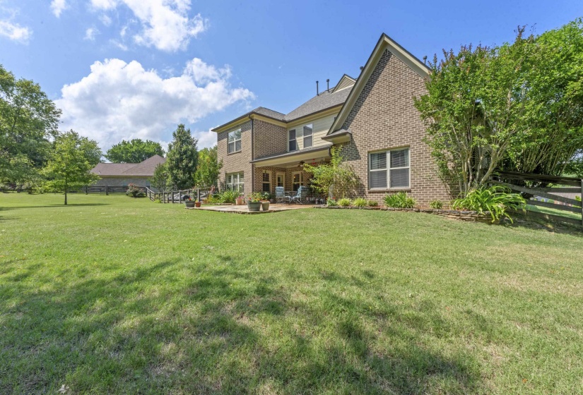 Impressive rear elevation showcasing the spacious covered patio, manicured landscaping, and expansive yard perfect for outdoor living.