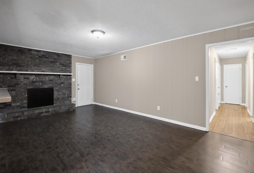Living area featuring dark wood-finish flooring, a black brick fireplace with a light-colored mantel, and light beige paneling on the walls