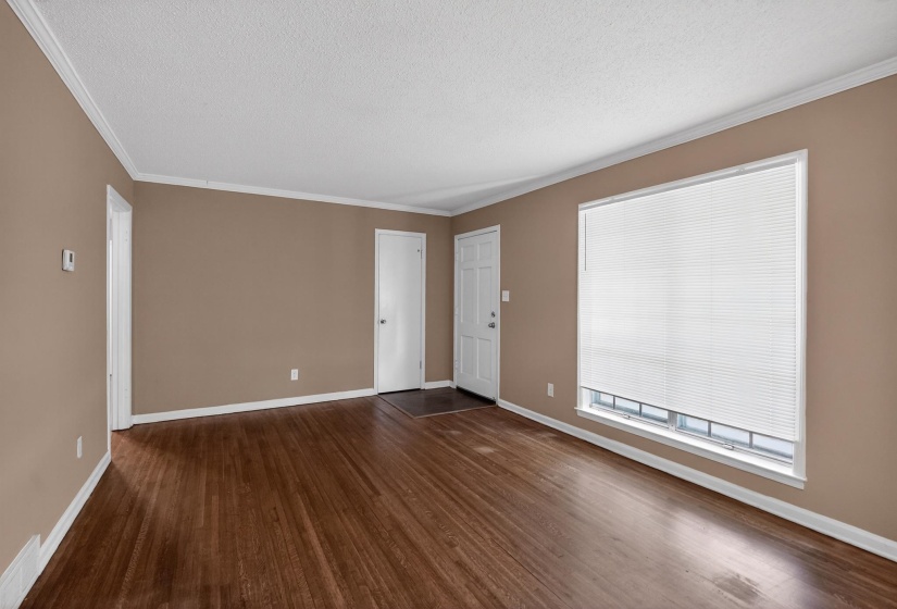 Spacious room featuring wood-finish flooring, a large window with blinds, and neutral-toned walls