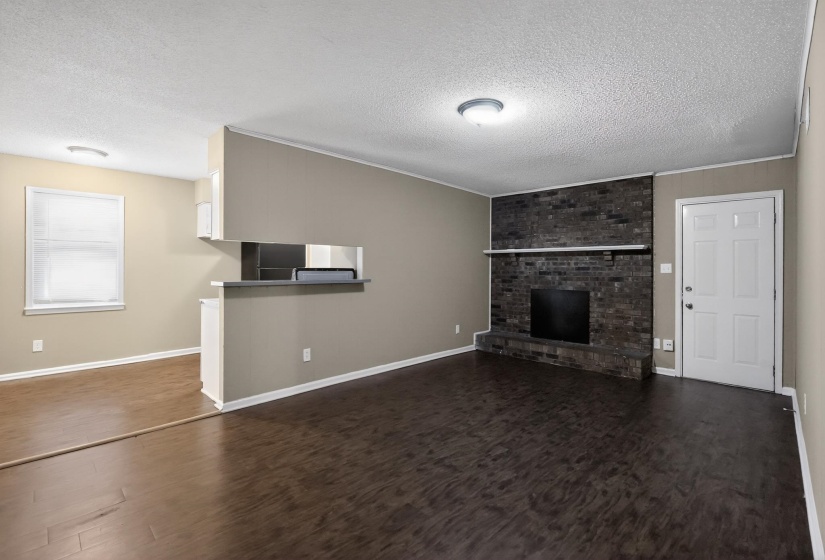 Living area featuring dark wood-finish flooring, a brick fireplace with a white mantel, and a pass-through opening to an adjacent space