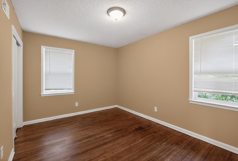 Room featuring wood-finish flooring, two windows with blinds, a ceiling-mounted light fixture, and a built-in closet with sliding doors