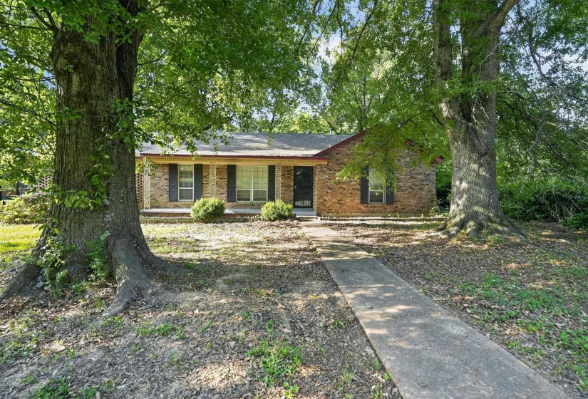 Brick facade residence featuring a covered front porch and mature trees