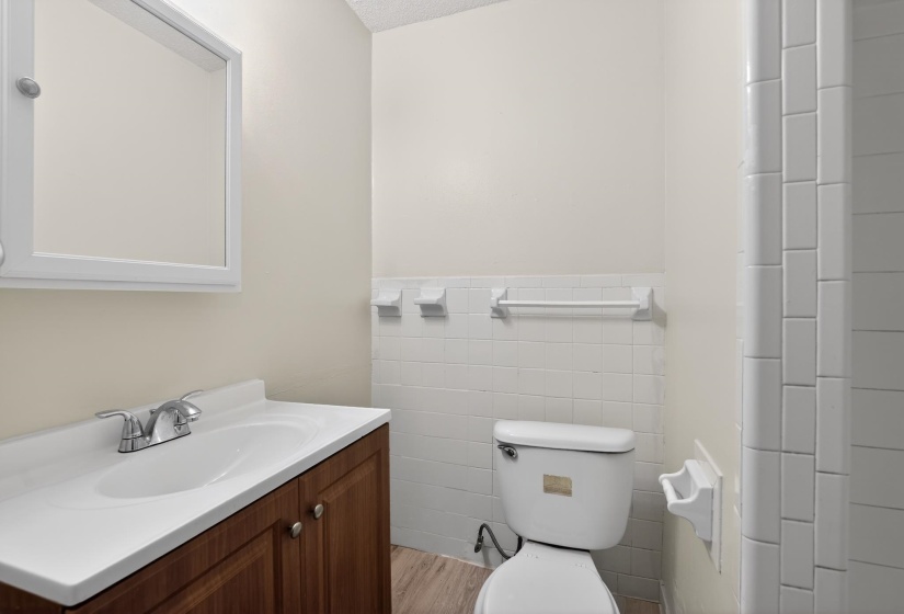 Bathroom featuring a wood-finish vanity with an integrated sink and chrome faucet, a wall-mounted medicine cabinet, white subway tile accents, and wood-finish flooring