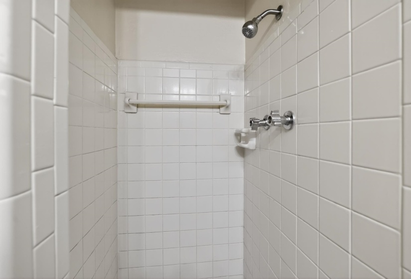 Shower stall featuring white square tile surround, chrome fixtures, and a wall-mounted showerhead