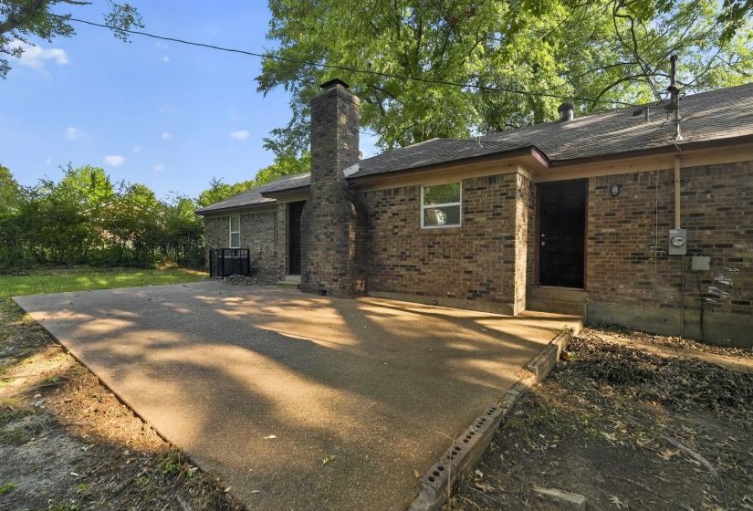 Expansive concrete patio with a brick exterior, prominent brick chimney, and a durable shingle roof