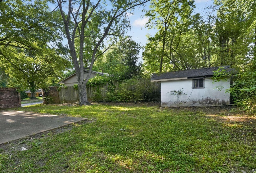 Expansive yard featuring a concrete patio, mature trees, and a detached storage shed with a single window